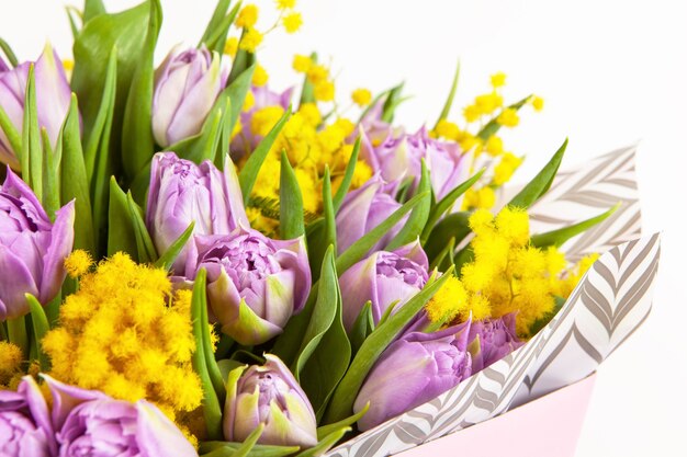 Bouquet of lilac tulips and yellow mimosas in pink box on white wall, closeup, side view. 