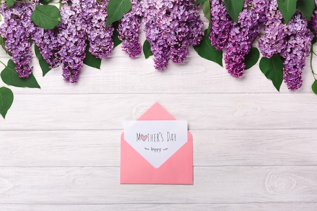 A bouquet of lilacs and color envelope with a love note on white boards . Mother's day