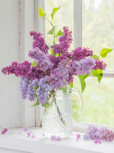 Bouquet of lilacs in a glass jug on old white windowsill