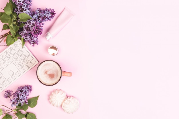 bouquet of lilacs, a keyboard, a cup of coffee, cakes, face cream on pink flat lay