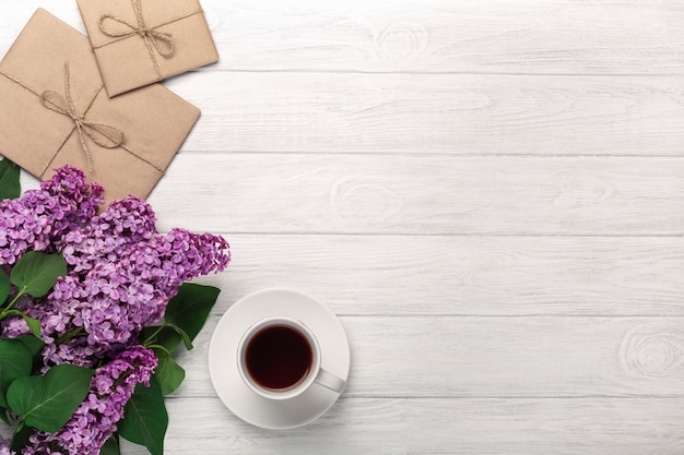 A bouquet of lilacs with cup of tea and craft envelopes on white boards . Mother's day