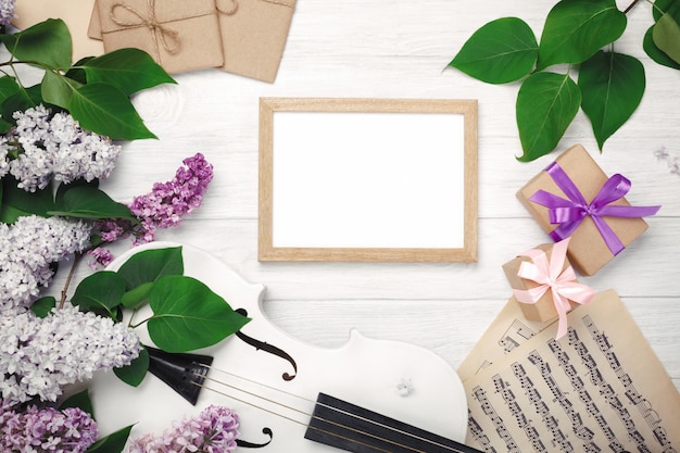 A bouquet of lilacs with violin, chalk board, gift box and music sheet on a white wooden table. Top wiev with space for your text