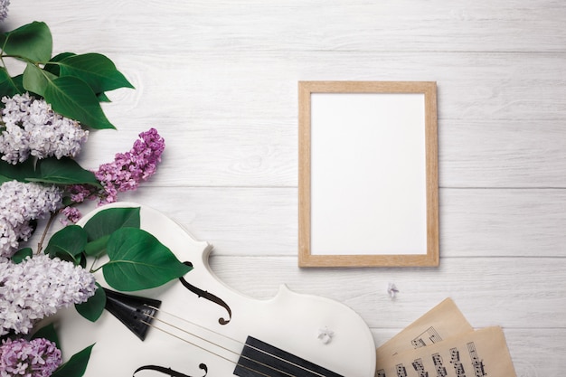 A bouquet of lilacs with violin, chalk board and music sheet on a white wooden table. Top wiev with space for your text