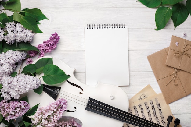 A bouquet of lilacs with violin, letter, notepad and music sheet on a white wooden table. Top wiev with space for your text