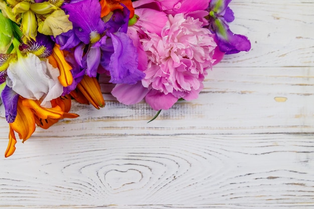 Bouquet of lilies peonies and iris flowers on a white wooden background Top view copy space