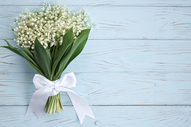 Bouquet of lilies of the valley with a white ribbon on a blue background