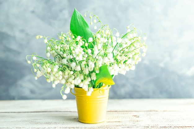 灰色の背景に黄色のバケツで谷のユリの花束