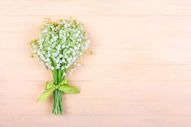 Bouquet di fiori di mughetto con un fiocco verde su uno sfondo rosa in legno con uno spazio di copia