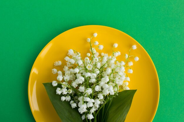 緑の背景の黄色いプレートにスズランの花束