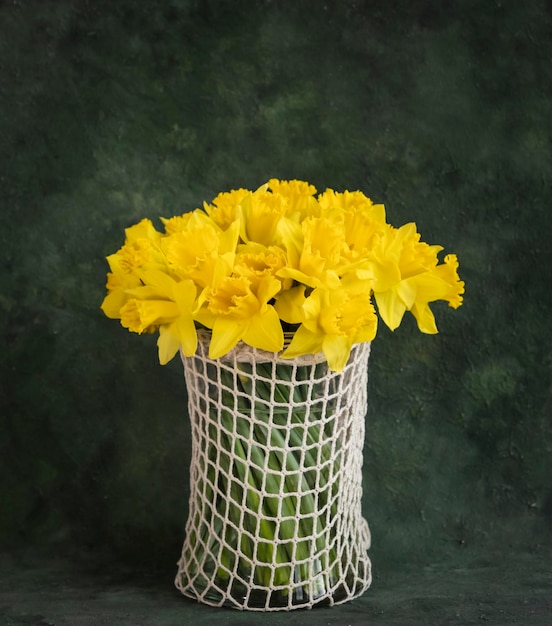 Bouquet di graziosi narcisi in vaso di vetro su sfondo verde vintage