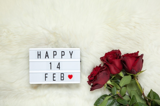 Bouquet di rose marrone rossiccio su tappeto di pelliccia bianco latte, lightbox con scritta happy 14 feb che significa san valentino. lay piatto. vista dall'alto.