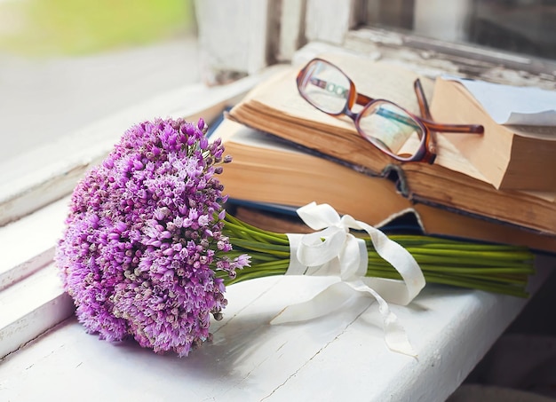 A bouquet of meadow flowers old books and glasses on a wooden windowsill