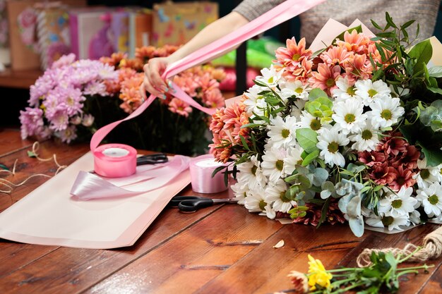 여러 가지 빛깔의 국화 꽃다발은 나무 테이블에 놓여 있습니다. 플로리스트가 꽃다발을 만드는 과정.
