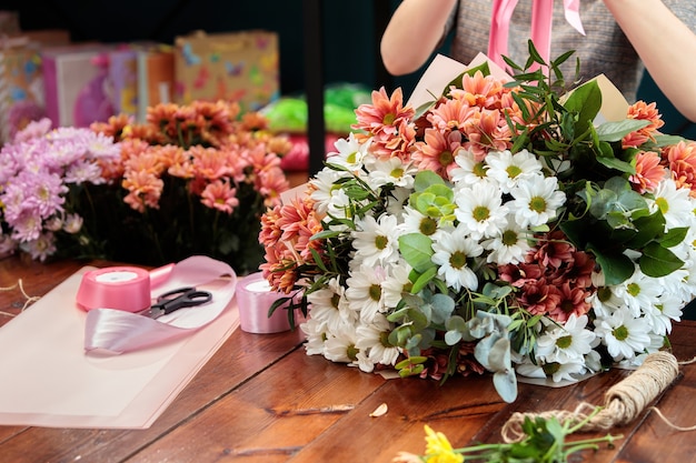 色とりどりの菊の花束が木製のテーブルの上にあります。花屋が花束を作る過程。