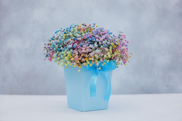 Foto bouquet di gipsofila multicolore in scatola blu con fiocco su sfondo grigio
