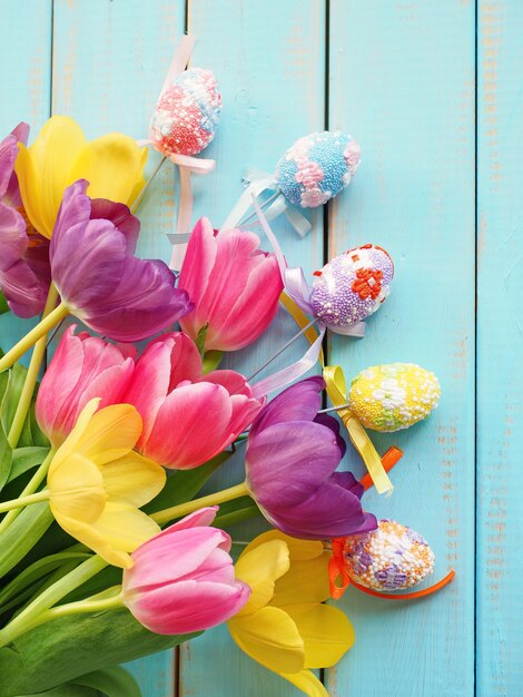 Bouquet of multicolored tulips with decorative Easter eggs on blue wooden surface