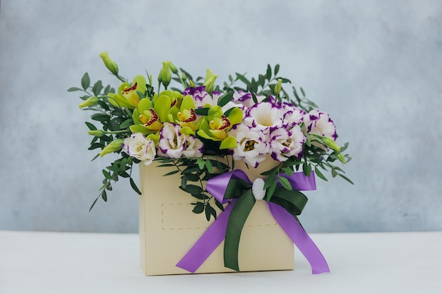 사진 보라색 흰색과 노란색으로 회색 배경에 종이 선물 상자에 archidea와 eustoma의 꽃다발