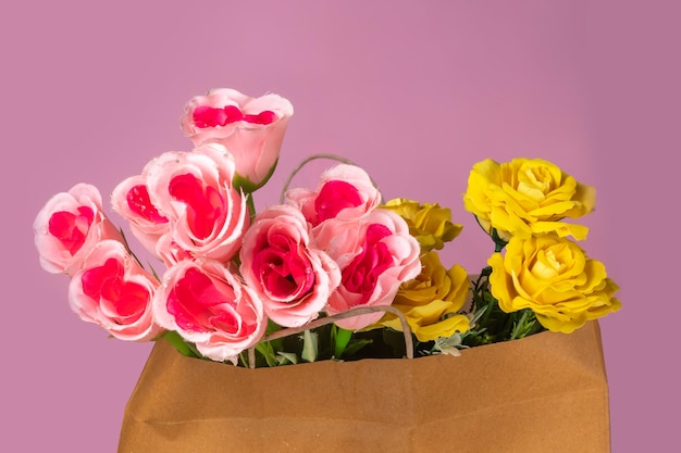 Фото Букет искусственных розовых и желтых роз в бумажном пакете на розовом фоне