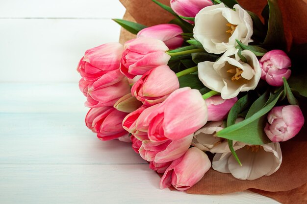Фото Букет нежных розовых тюльпанов в бумаге на светлом деревянном фоне пустая для вашего дизайна