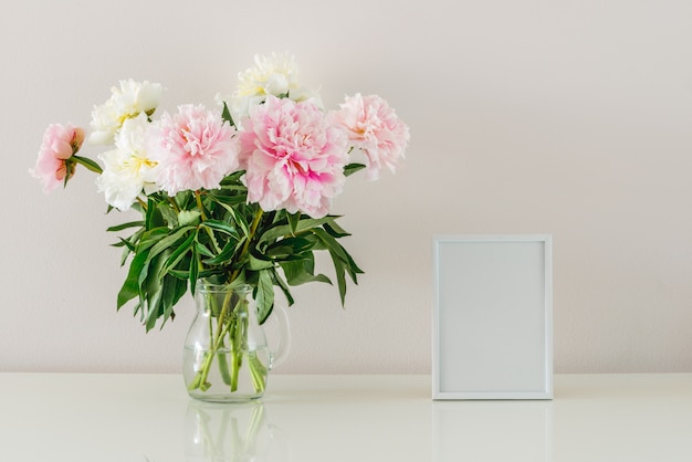 Bouquet of peonies and white frame with copy space on white