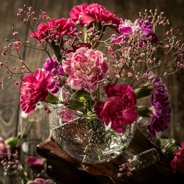 古い木の表面のガラスの花瓶のピンクのカーネーションの花束。母の日、誕生日グリーティングカード