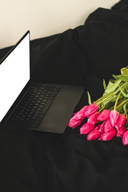 A bouquet of pink flowers on black stylish linen with an open laptop