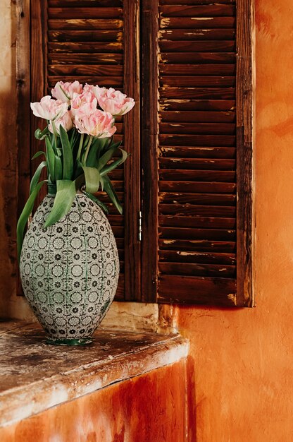 bouquet of pink flowers in an old big vase on a window sill