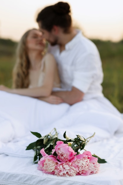 Bouquet of pink flowers on a white bed, in the background a couple kisses