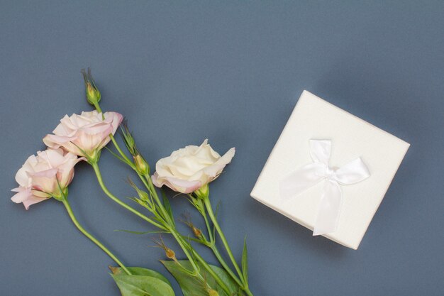 Bouquet of pink flowers with leaves and gift box on gray background. Top view. Celebration day concept.