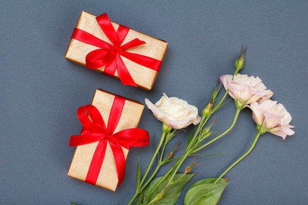 Bouquet of pink flowers with leaves and gift boxes with red ribbons on gray background. Top view. Celebration day concept.