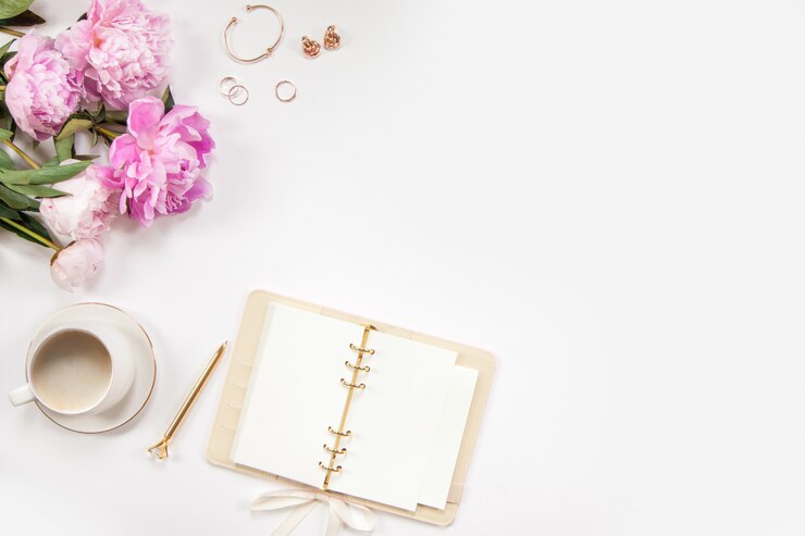 Photo a bouquet of pink peonies, a gold pen, women's jewelry and a diary on a white background. coffee in a white mug. copy space.