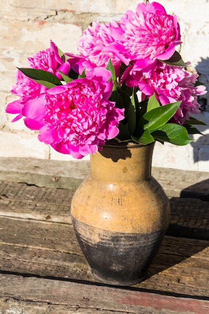 Bouquet of pink peony flowers in clay jug on rustic wooden table