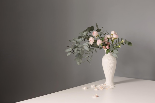 Bouquet of pink roses in ceramic white vase on background gray wall