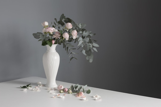 Bouquet of pink roses in ceramic white vase on background gray wall