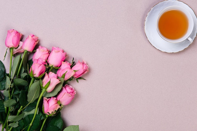 bouquet of pink roses and cup of tea on pink backround. flat lay with copy space.