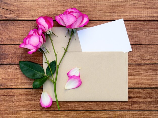 木製の背景の封筒にピンクのバラの花束。デザインの場所が書かれたはがき。