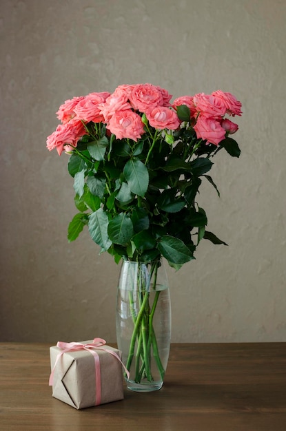 Bouquet of pink roses in a glass vase with gift box on a wooden table stilllife Mother's day Val
