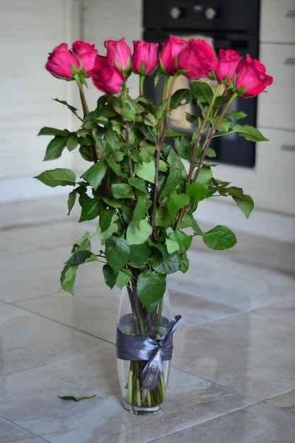 A bouquet of pink roses is in a vase on the floor