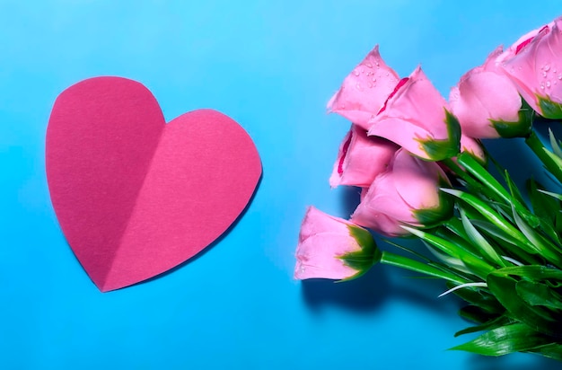 Bouquet of pink roses and red paper heart on blue background