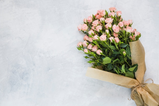 Bouquet of pink roses wrapped in brown paper with string on concrete wall