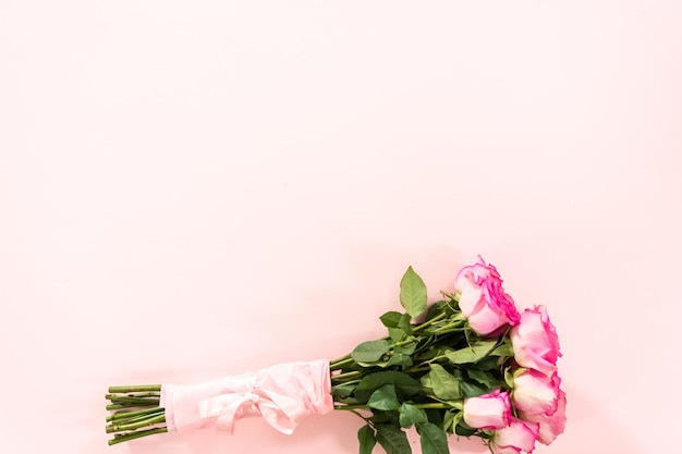 Bouquet of pink roses wrapped in pink wrapping paper with a pink ribbon on a pink background