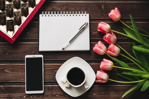 Bouquet di fiori di tulipano rosa con una tazza di caffè e una scatola di cioccolatini e un taccuino vuoto con uno smartphone