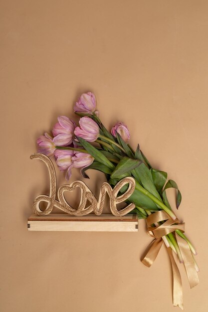 a bouquet of pink tulips on a beige background and a wooden craft inscription love a place for text