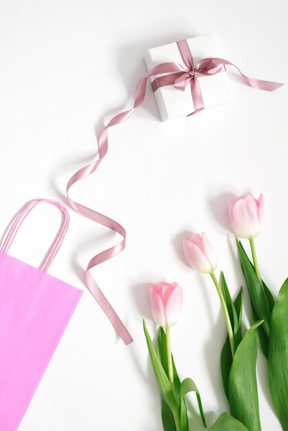 A bouquet of pink tulips a gift box with a pink bow and a pink bag on a white background