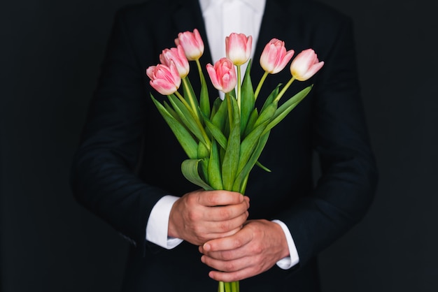 Bouquet of pink tulips in men's hands in a blue suit