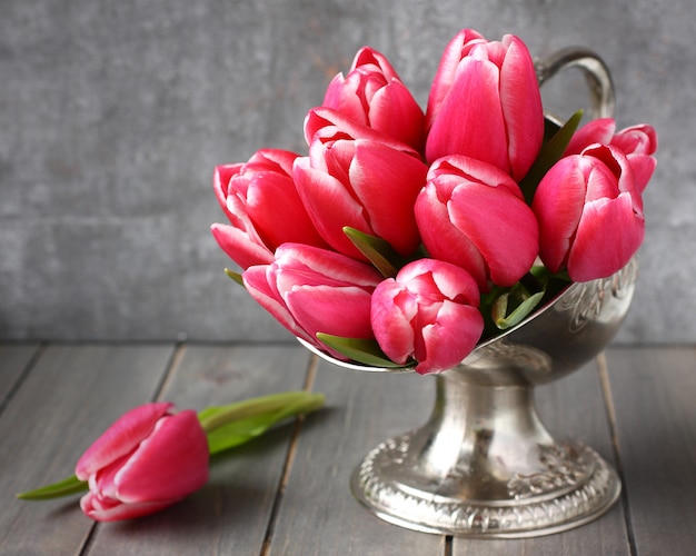 Bouquet of pink tulips in metal vase on wooden background