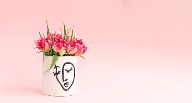 Bouquet of pink tulips in a white vase on a pink background