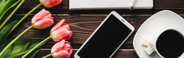 Bouquet of pink tulips with a Cup of coffee and a smartphone on a wooden table