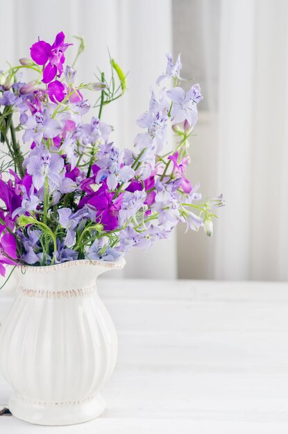 白い木製のテーブルの上のジャグで紫色のルピナスの花の花束