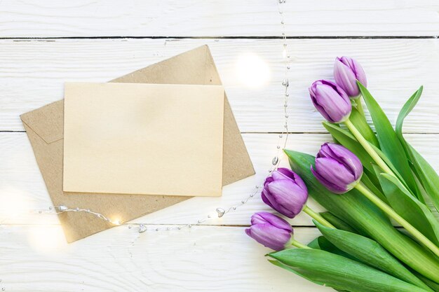 Bouquet of purple tulips and blank greeting card on white wooden background top view copy space